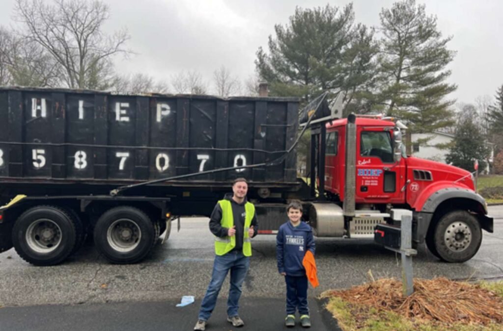 A Hiep Sanitation worker setting up a residential-sized dumpster in a Bergen County driveway, demonstrating ease of service and readiness to assist with home renovation cleanups, Dumpster Rental Near Me.